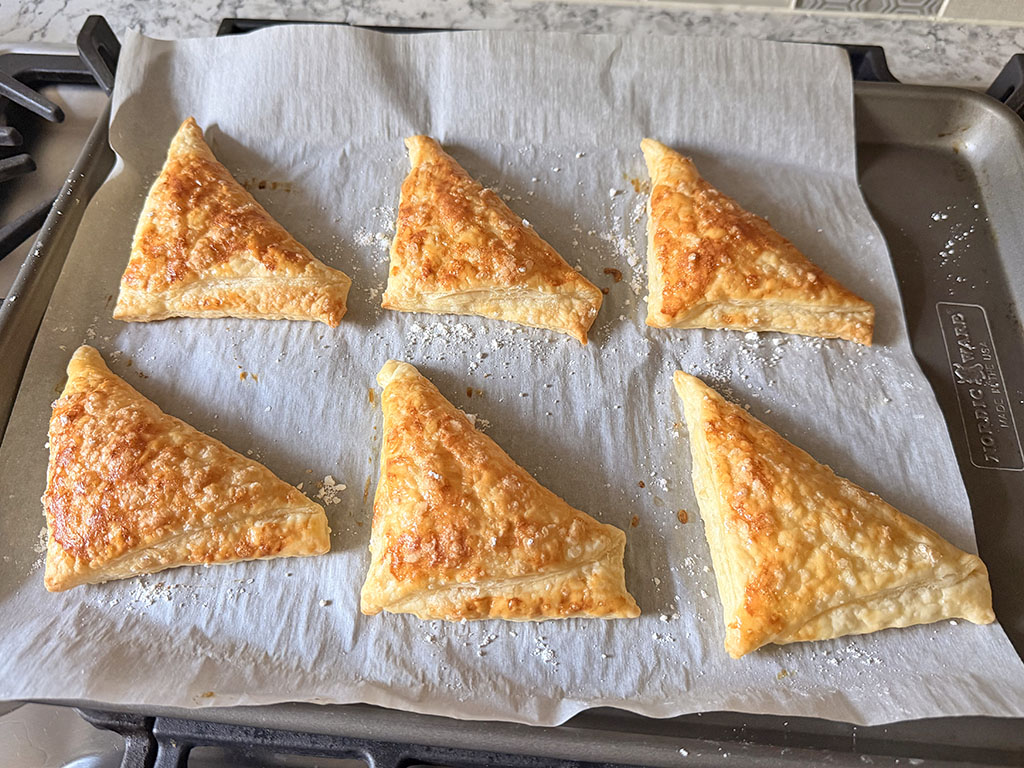 Golden baked puff pastry triangles on a baking sheet.