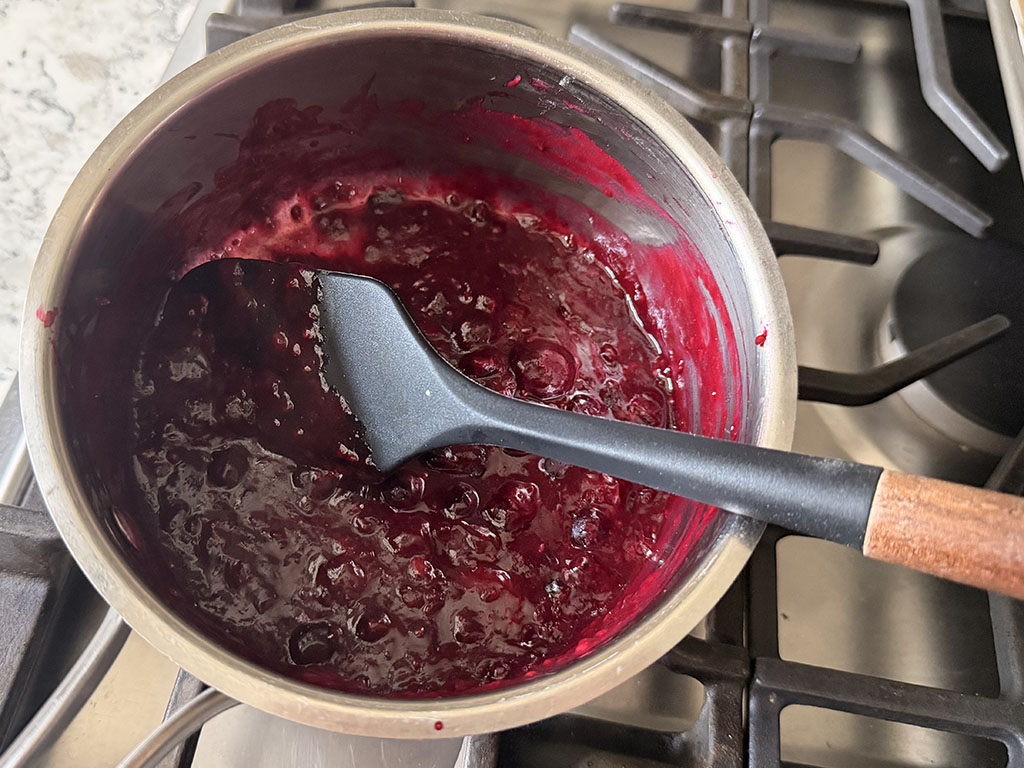 Berry sauce in a saucepan, stirred with a spatula.
