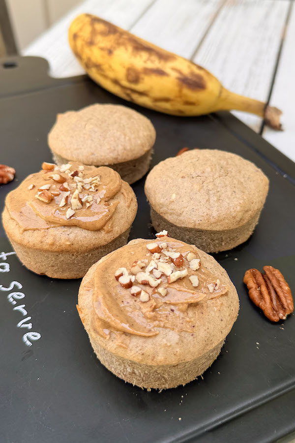 Gluten Free Banana Oat Muffins on e serving platter, a couple of muffins are spreaded with peanut butter and topped with chopped pecans