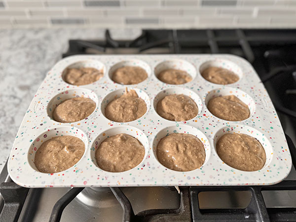 Muffin batter distributed between silicone muffin tin cups.
