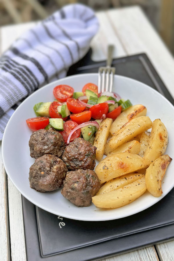 Greek bowl with potatoes, meatballs and fresh salad in a shallow dish with a fork.