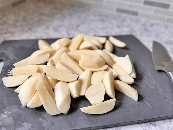 Potatoes cut into wedges on a cutting board.