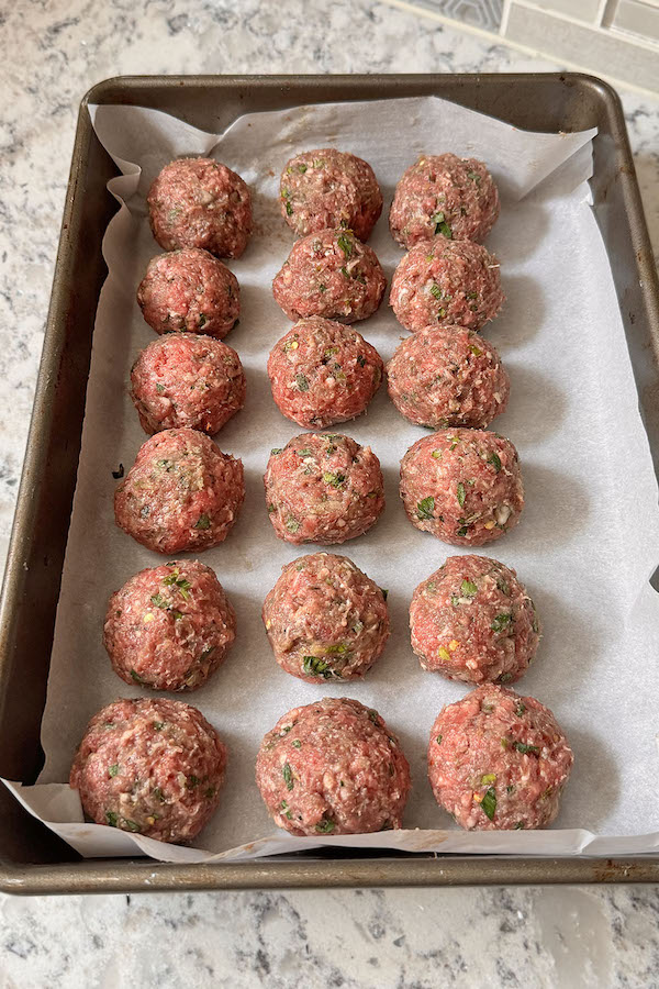 Formed raw meatballs on a baking sheet lined with parchment paper.