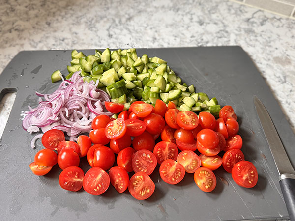 Prepared salad ingredients: diced cucumbers, halved grape tomatoes, and thinly sliced onion.