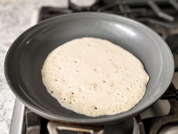 Cottage cheese and oat tortilla cooking in a skillet on the first side.