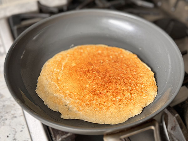 Beautiful golden brown cottage cheese and oat tortilla cooking in a skillet on the other side.