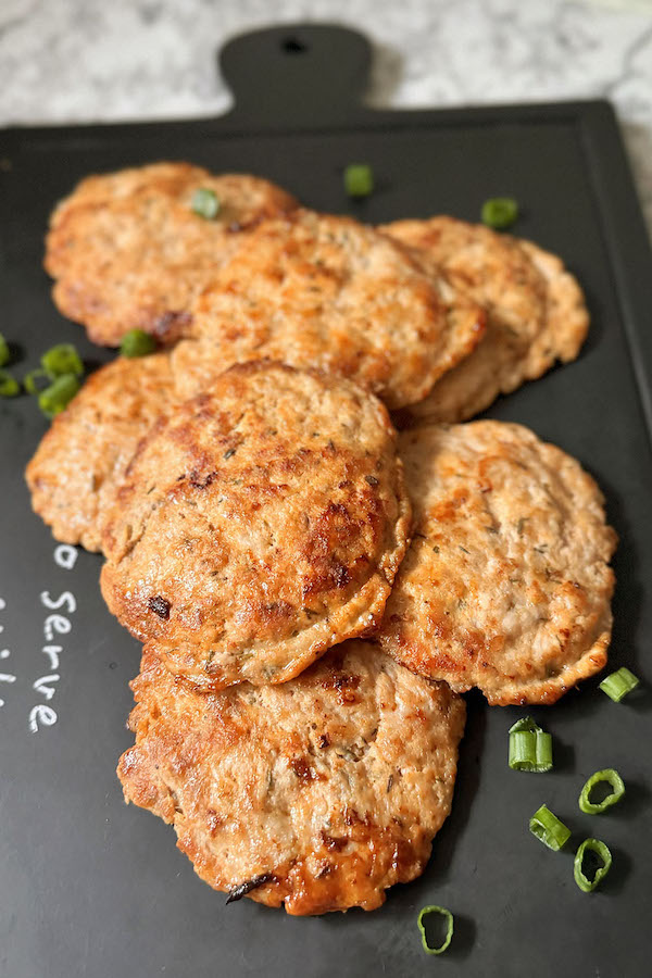 Homemade Pork Breakfast Sausage patties on a serving board with chopped green onions on the side.