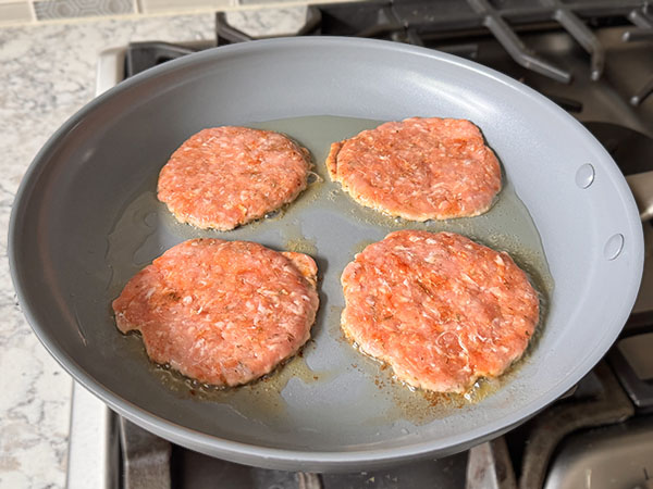 Pork breakfast sausage patties cooking in a skillet on first side.