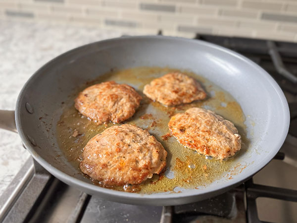 Golden brown pork breakfast sausage patties cooking in a skillet on the second side.