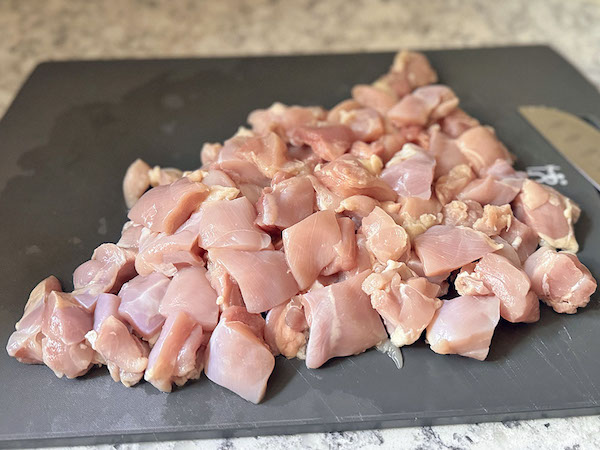 Raw chicken thighs cut into bite-sized pieces on a cutting board.