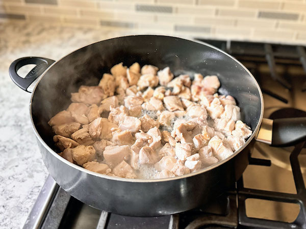 Chicken thighs pieces cooking in a large skillet on the stove top.