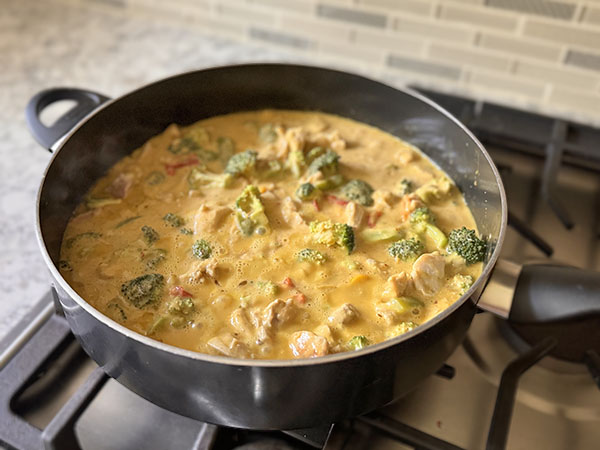 Mango chicken curry with broccoli and bell peppers, simmering on the stove top.