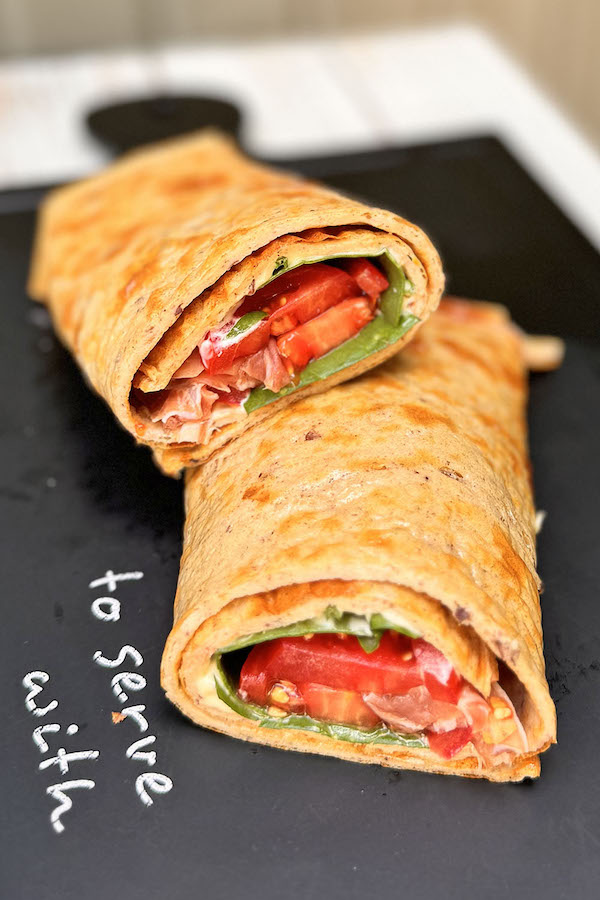 Mediterranean Cottage Cheese Wrap with Prosciutto & Spinach on a serving board, cut in half to show the filling.