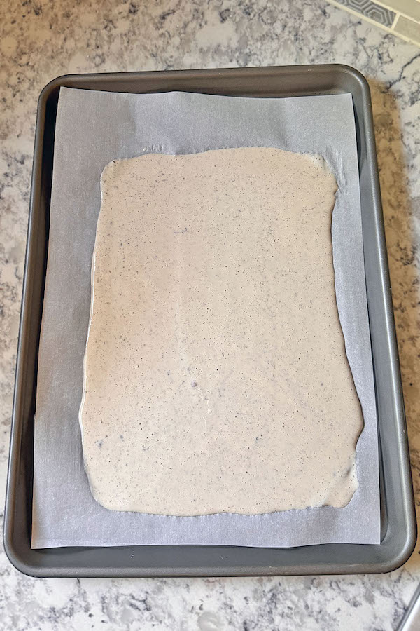 Cottage cheese wrap batter spread on a parchment lined baking sheet.