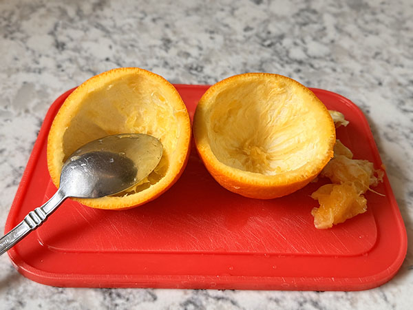 Половинки апельсина с вырезанной мякотью на разделочной доске.