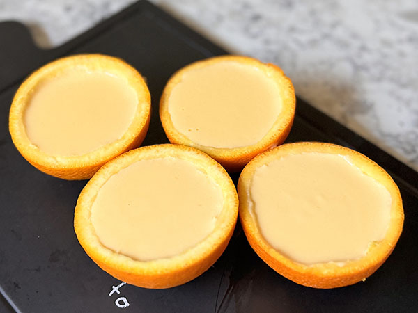 Половинки апельсина, наполненные апельсиновым заварным кремом, на сервировочной доске.