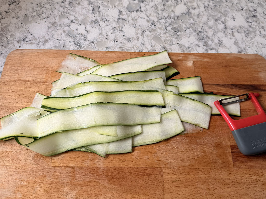 Zucchini ribbons on a cutting board with a vegetable peeler.