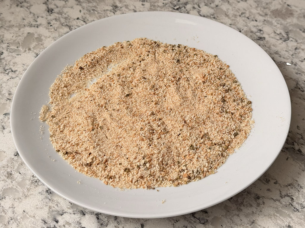 Breadcrumbs mixed with oregano and salt on a large plate.
