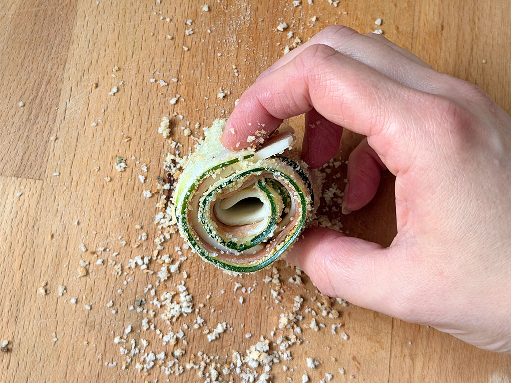 Zucchini roll-up held in hand before baking.