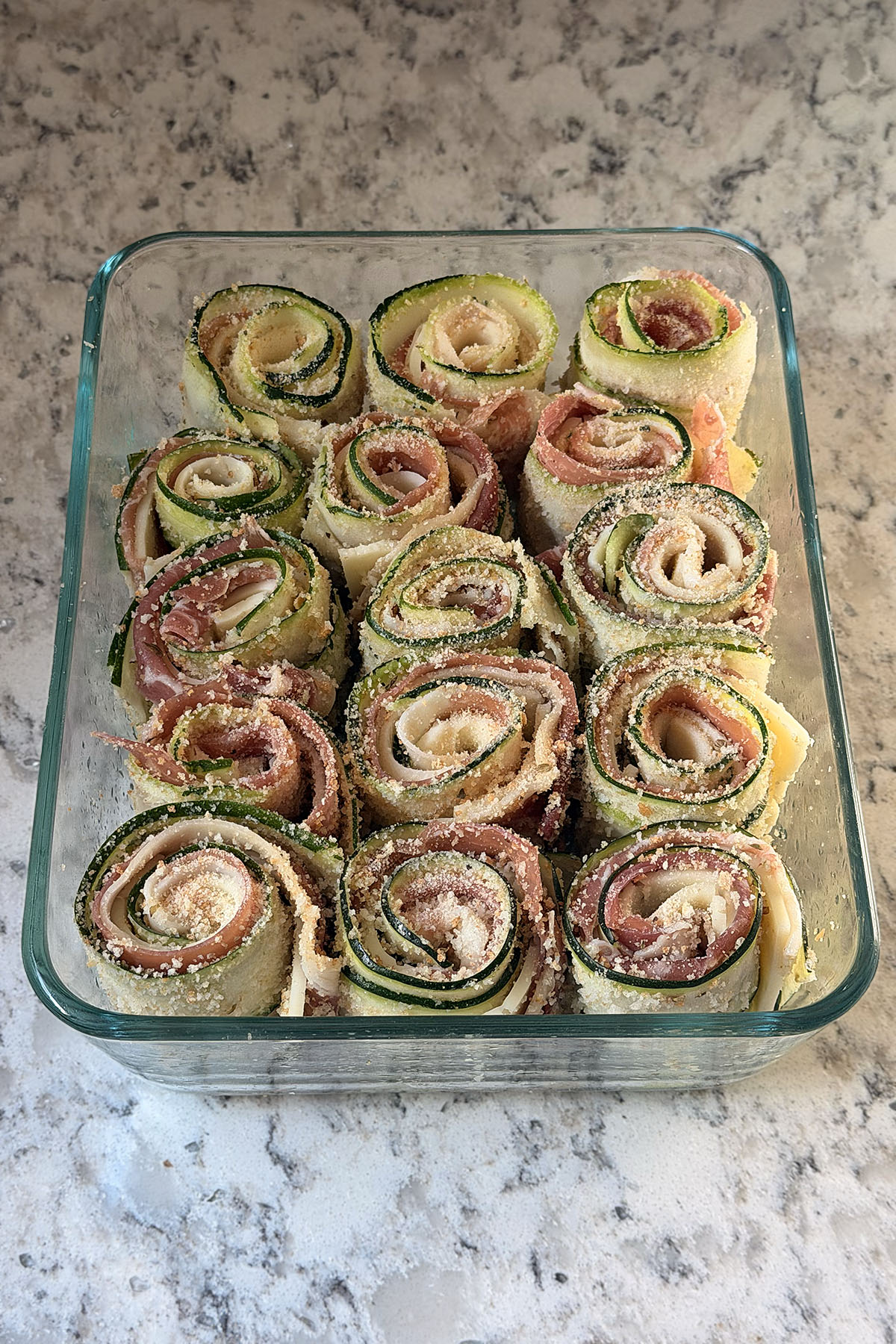 Zucchini roll-ups placed snugly next to each other in a baking dish in a single layer.