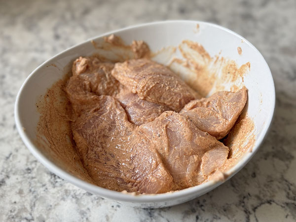 Chicken pieces covered in yogurt marinade in a bowl.