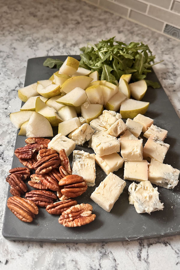 Ingredients for the blue cheese pear appetizer: fresh pear, arugula, blue cheese and pecans on a cutting board.