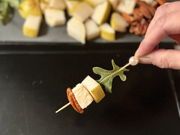 Hand holding Pear and Blue Cheese Skewer with Arugula and Pecans.