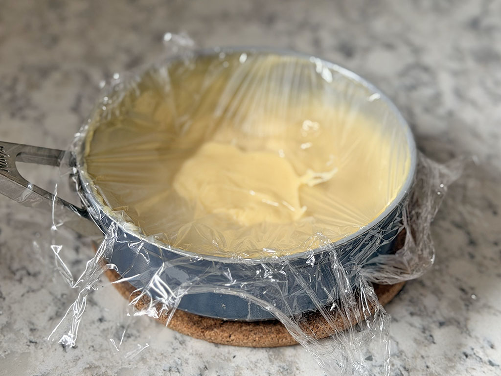 Готовый ванильный крем накрыт пищевой плёнкой в контакт, чтобы не образовалась корочка.