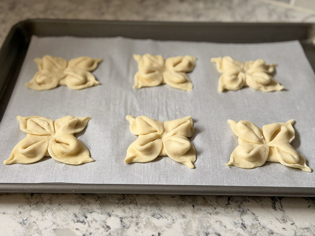 Заготовки из слоёного теста в форме цветочков выложены на противень с пергаментом.