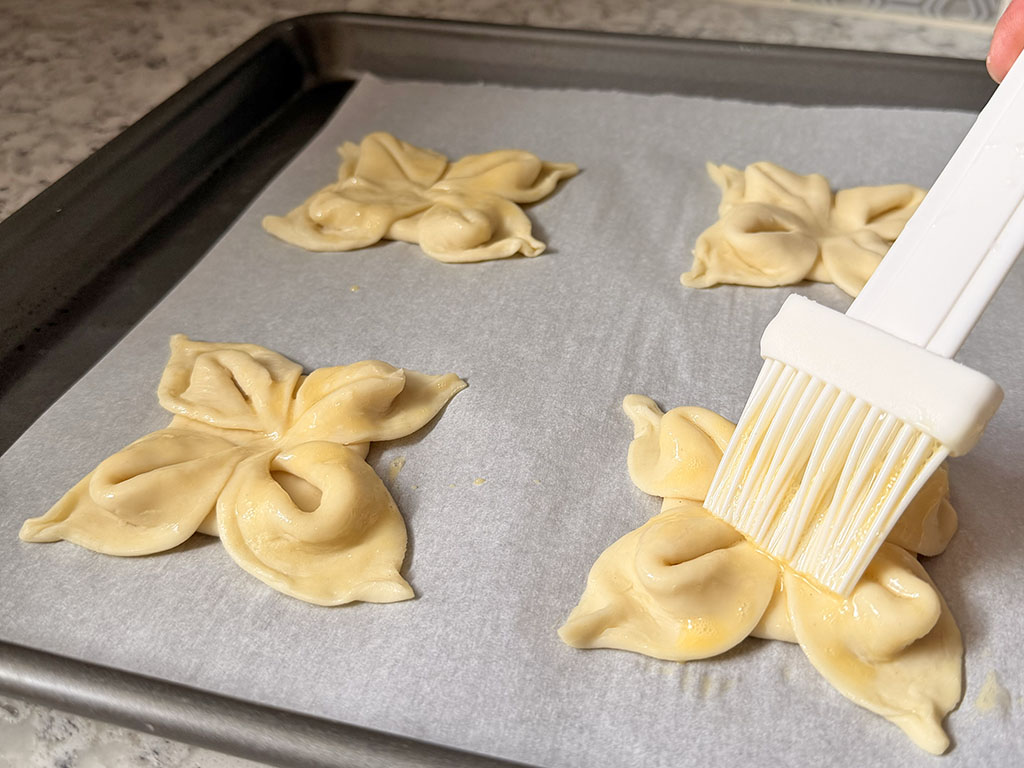 Цветочки из слоёного теста смазывают желтком перед выпеканием.