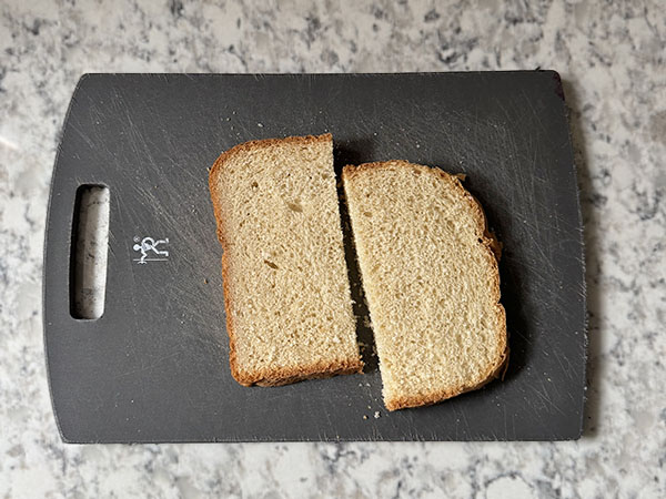 A slice of bread cut in half on a cutting board.