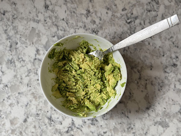 Avocado mashed with a fork in a small bowl.