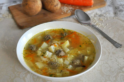 A bowl filled with Russian Meatball Soup with fresh vegetables and rice on the background.