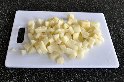 Potatoes cut into bite-sized cubes on a cutting board.