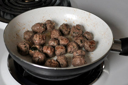 Ground beef meatballs searing in a skillet.