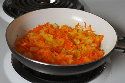 Onions and carrots searing in a skillet.