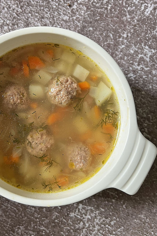 A bowl of Russian Meatball Soup (aka soup s frikadelkami) topped with fresh dill.