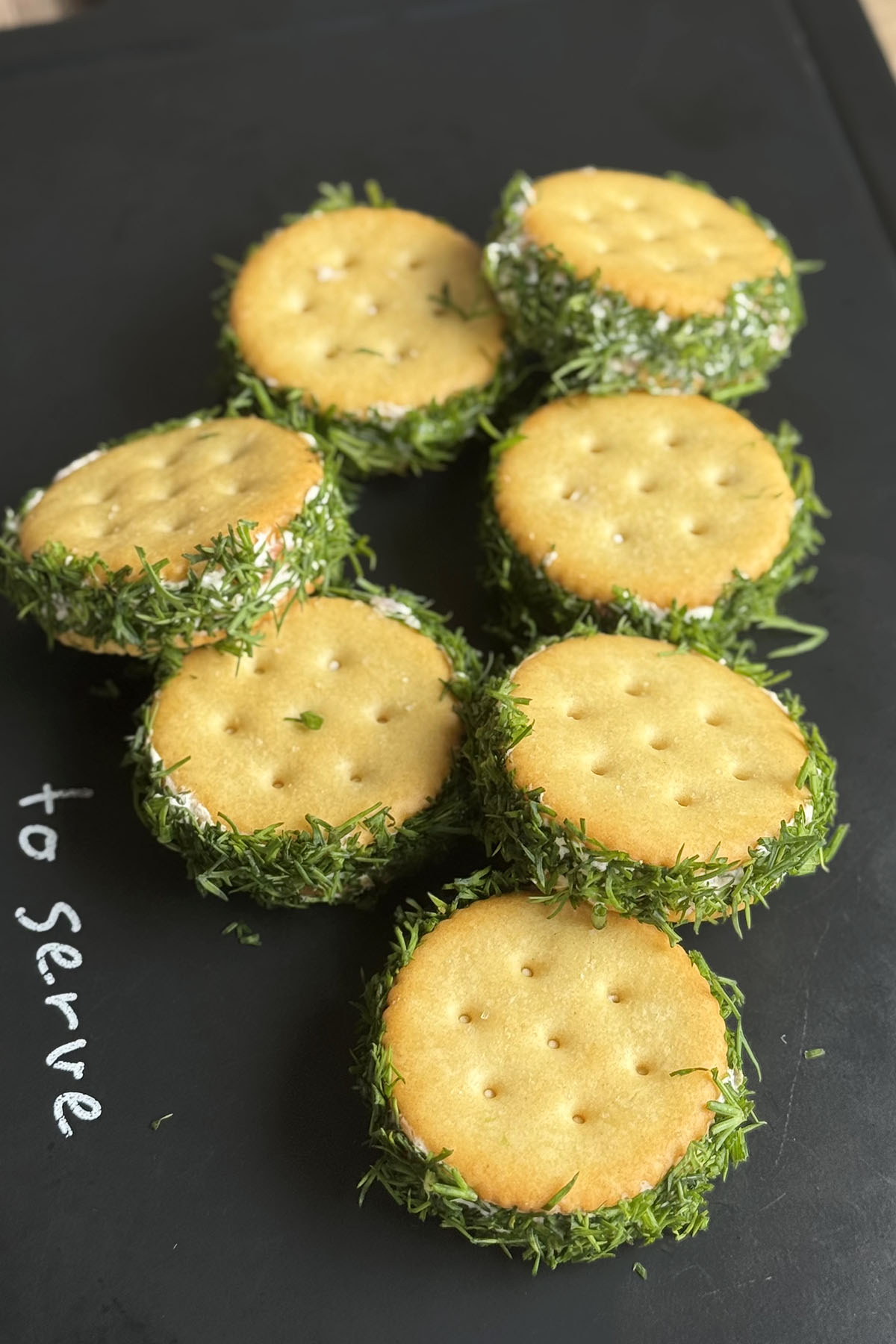 Smoked salmon and cream cheese cracker bites rolled in fresh dill on a serving board.