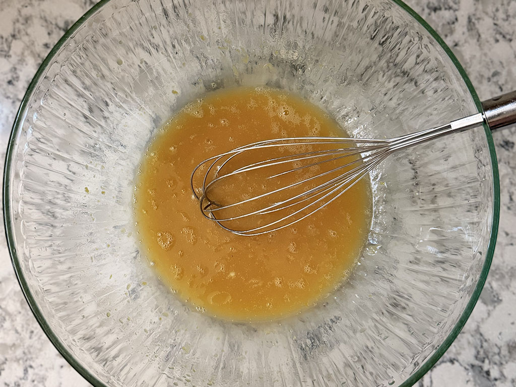 Whisking egg, maple syrup, avocado oil, lemon zest, lemon juice, and vanilla extract in a large bowl.