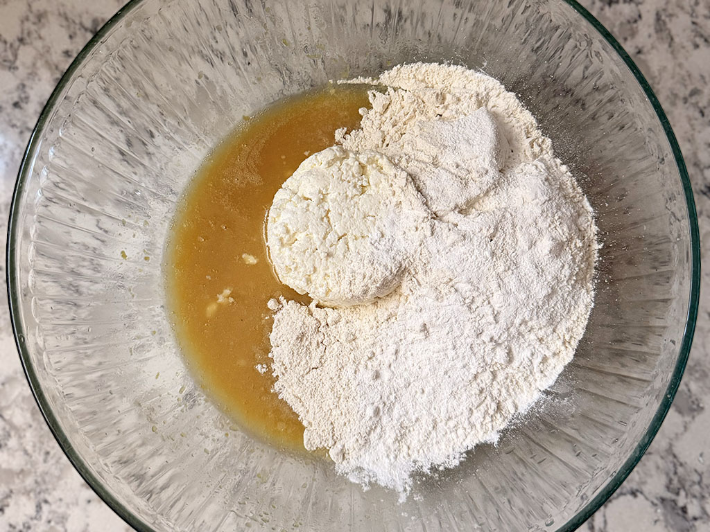 Adding farmer’s cheese, flour, baking powder, and salt to the wet ingredients in a large bowl.