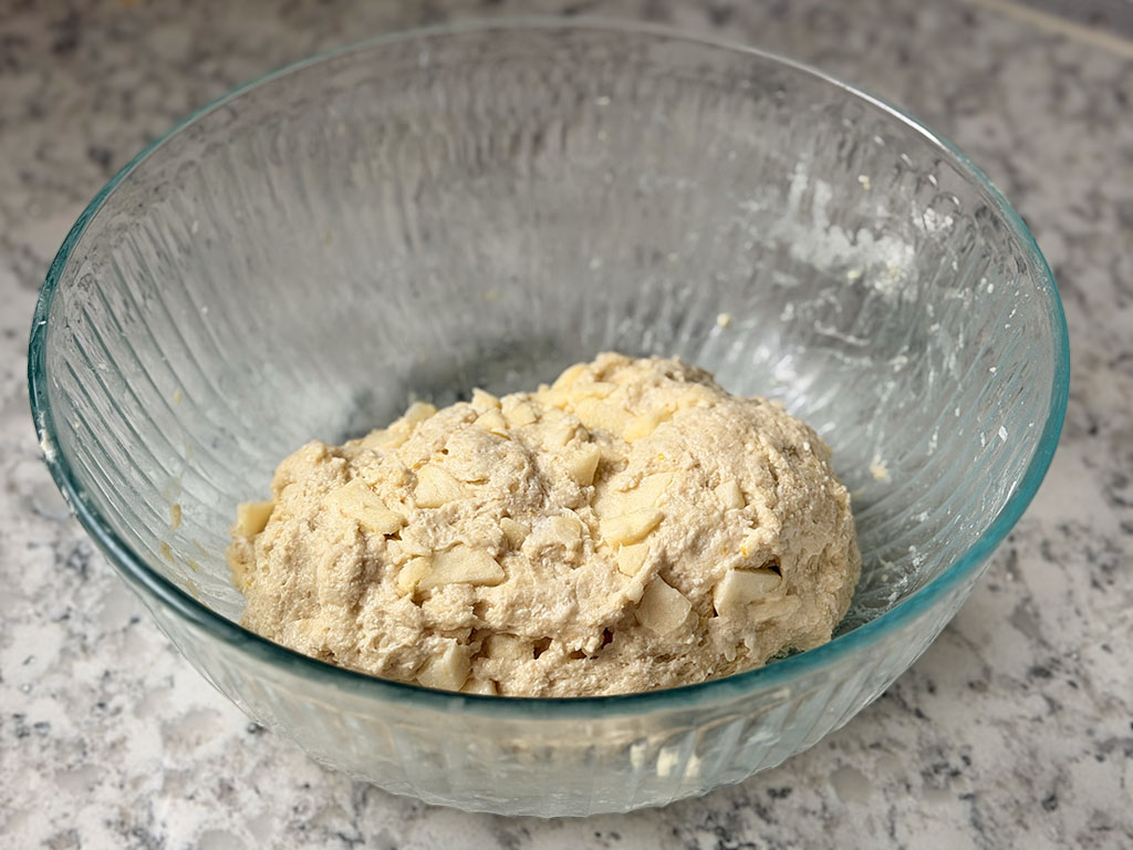 Soft cookie dough mixed with finely diced apples in a bowl.