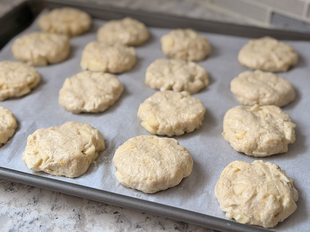 Slightly flattened raw cookie dough pieces arranged on a parchment-lined baking sheet.