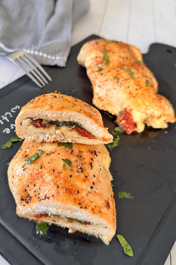 Baked chicken stuffed with spinach, mozzarella & sun-dried tomatoes on a serving board, cut in half to expose the filling.