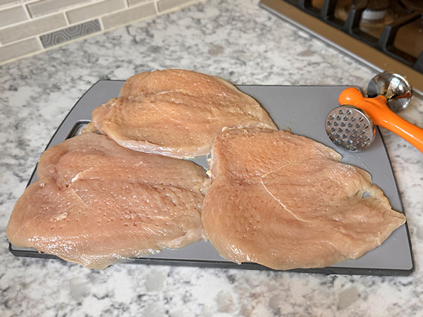 Raw chicken breasts pounded to an even thickness on a cutting board.