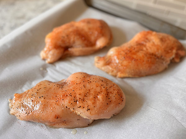 Closed stuffed chicken breasts seasoned with spices, drizzled with oil, on a baking sheet.