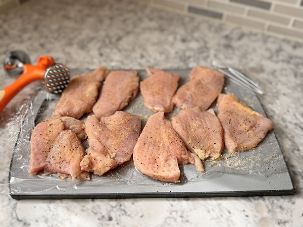 Chicken pieces pounded to even thickness on a cutting board.