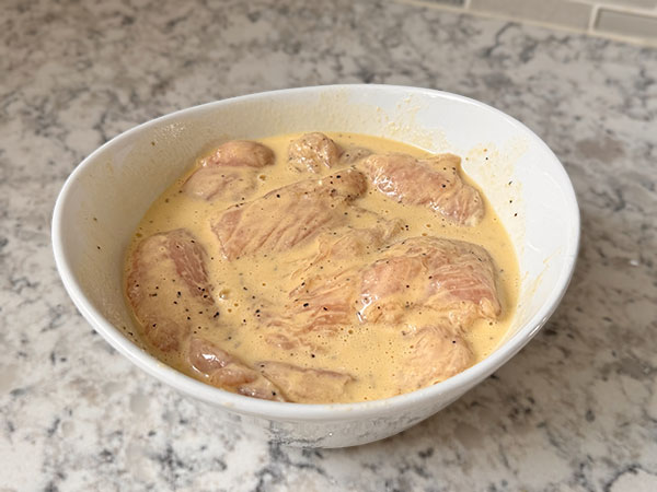 Chicken cutlets in mustard-mayo marinade in a bowl.