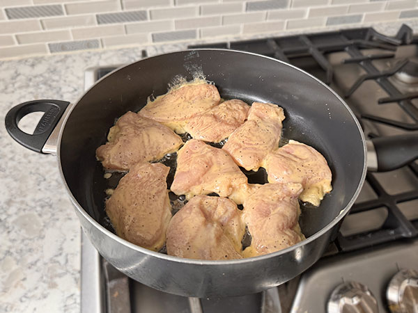 Marinated chicken cutlets cooking in a skillet on the first side.