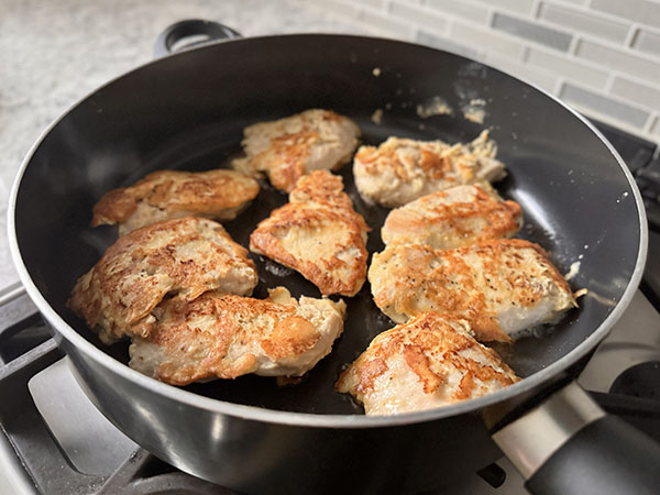 Golden brown chicken cutlets cooking in a skillet on the second side.