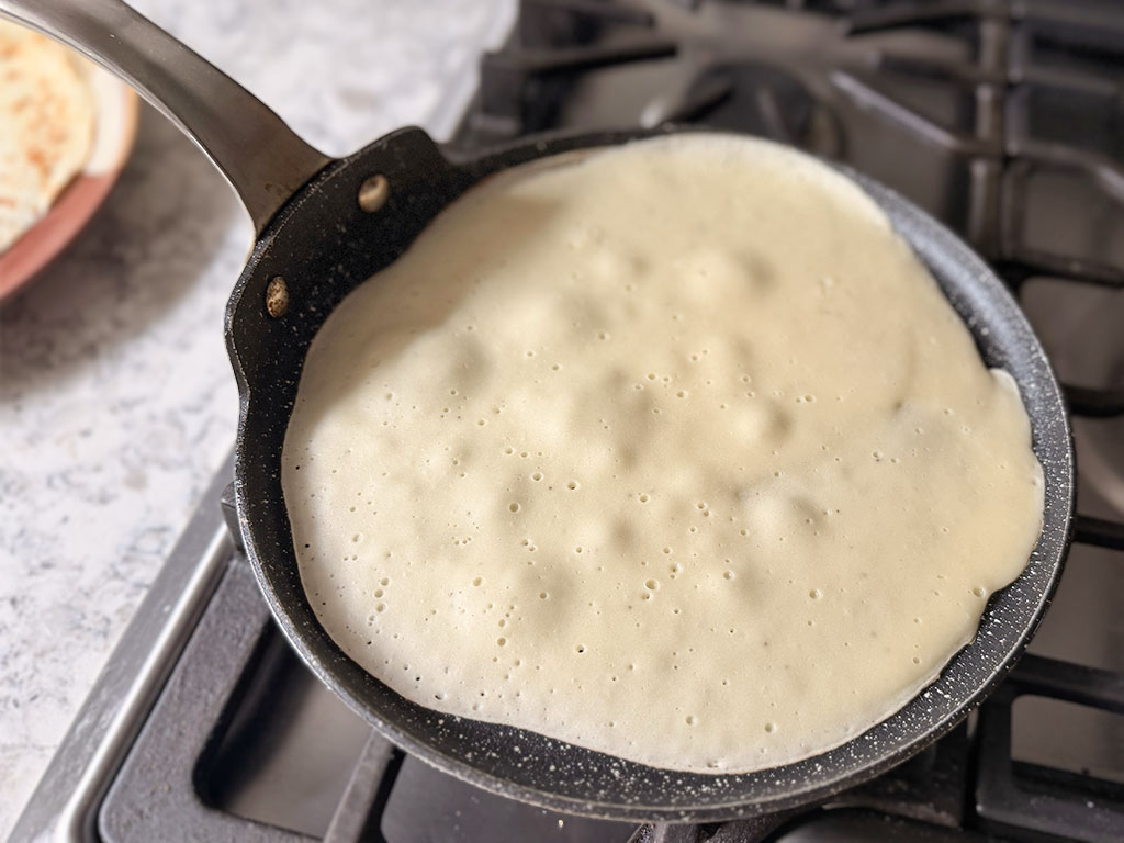 Banana crepe batter spread in a lightly oiled skillet and cooked until bubbles form on top.